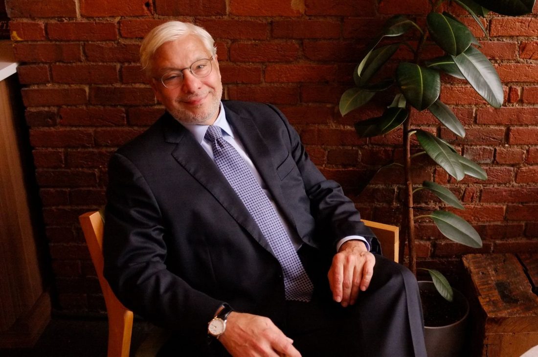 Gabriel Ramsey in a suit and tie, seated against a brick wall.