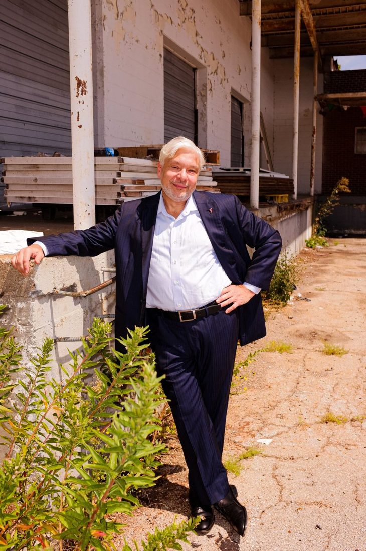 Gabriel Ramsey outdoors, leaning against a low wall among plants.