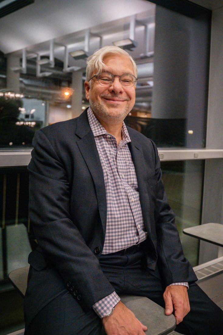 Gabriel Ramsey seated in a glass-walled building in the evening, smiling.